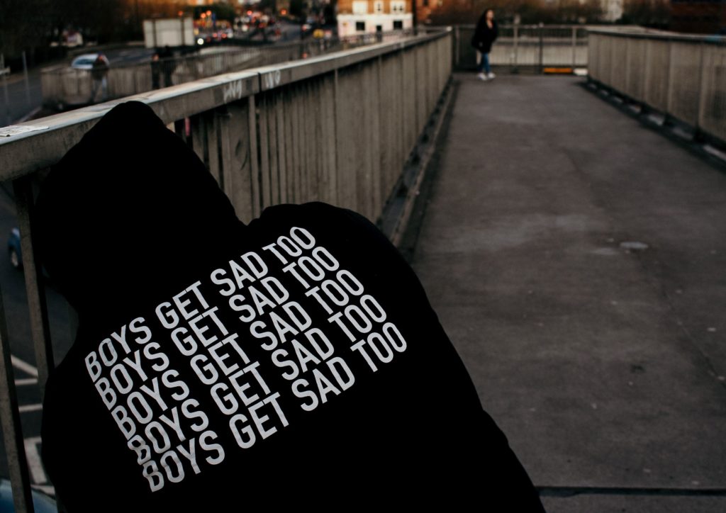 male wearing a sweatshirt that says "boys get sad too"